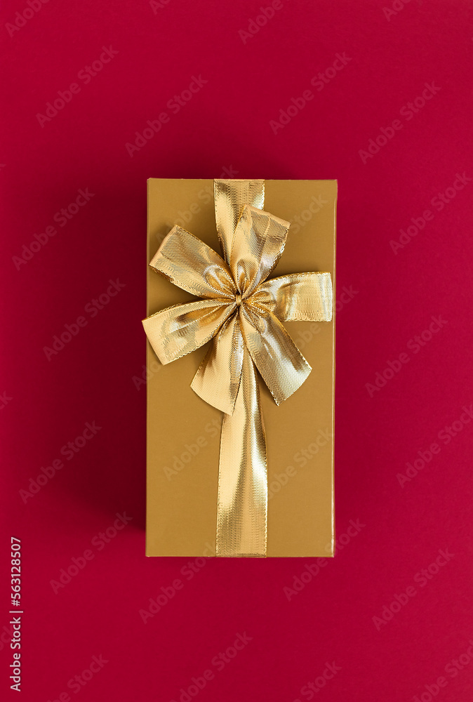 Golden gift box with golden ribbon and bow on a burgundy background. Top view. Copy space. Golden gift box with golden ribbon and bow on a burgundy background. Top view. Copy space.