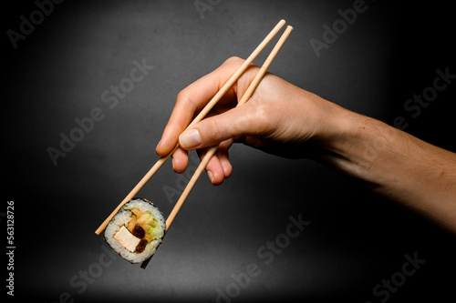 female hand accurate holds unagi sushi roll with smoked eel with chopsticks on dark background