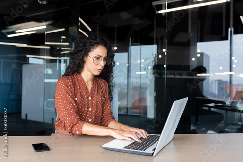 Serious young hispanic woman working in the office on a laptop. Concentrated typing on the keyboard, copying.