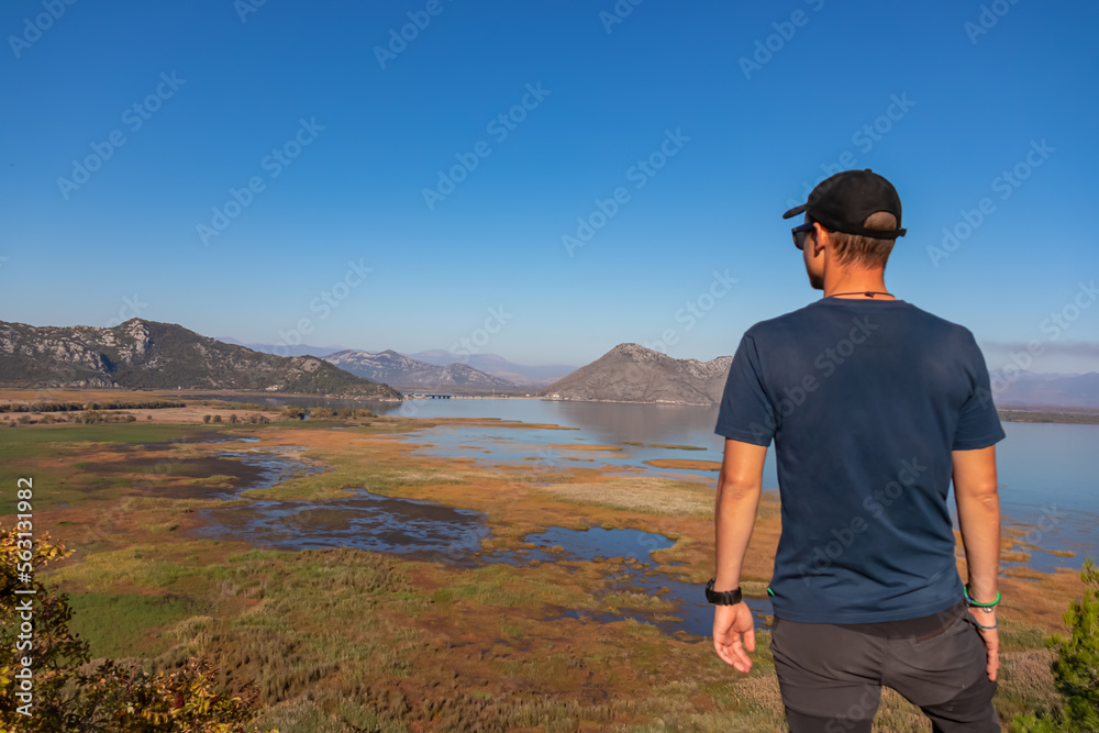 Rear view of man with panoramic view of Lake Skadar National Park in autumn seen from Virpazar, Bar, Montenegro, Balkans, Europe. Stunning travel destination in Dinaric Alps near Albanian border