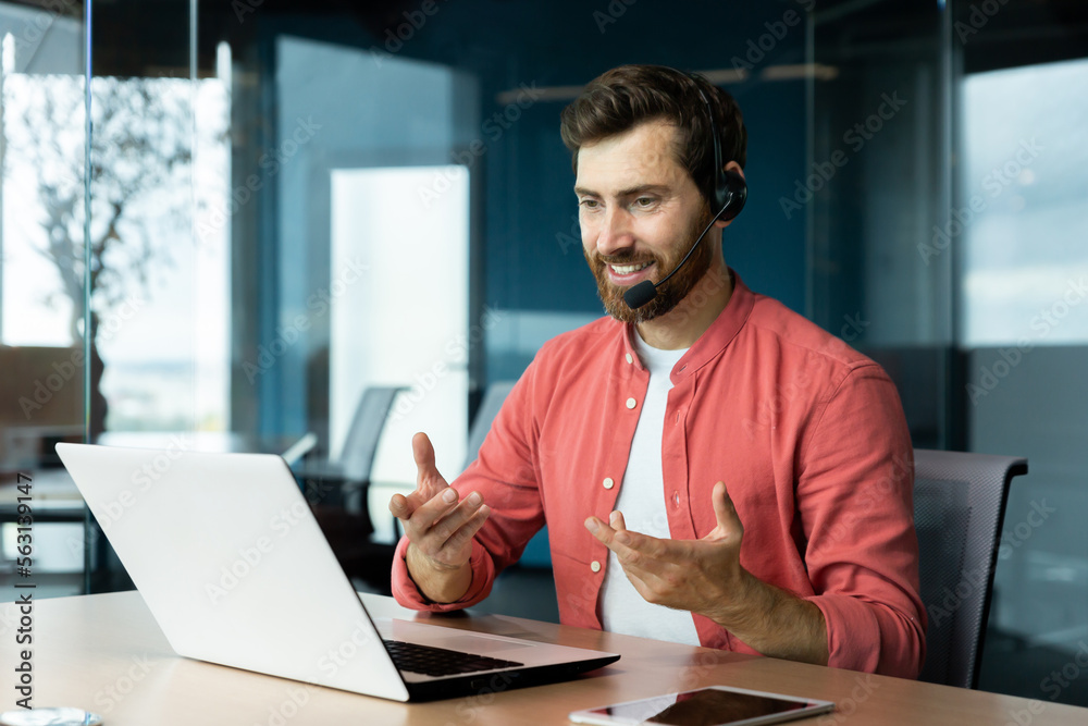 Mature successful businessman with video call headset working inside office, man consulting online clients, talking with colleagues on online remote meeting, sitting at workplace with laptop. - obrazy, fototapety, plakaty 
