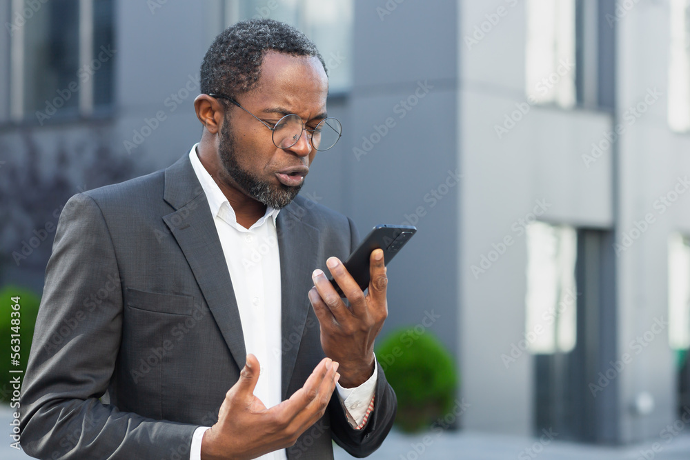 Angry and angry boss talking and shouting on mobile phone, african american businessman in business suit walking outside office and talking with subordinates. Angry and angry boss talking and shouting on mobile phone, african american businessman in business suit walking outside office and talking with subordinates.