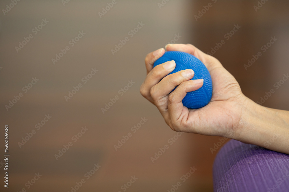 Hands of a woman squeezing a blue stress ball on the yoga mat for work out at home Hands of a woman squeezing a blue stress ball on the yoga mat for work out at home