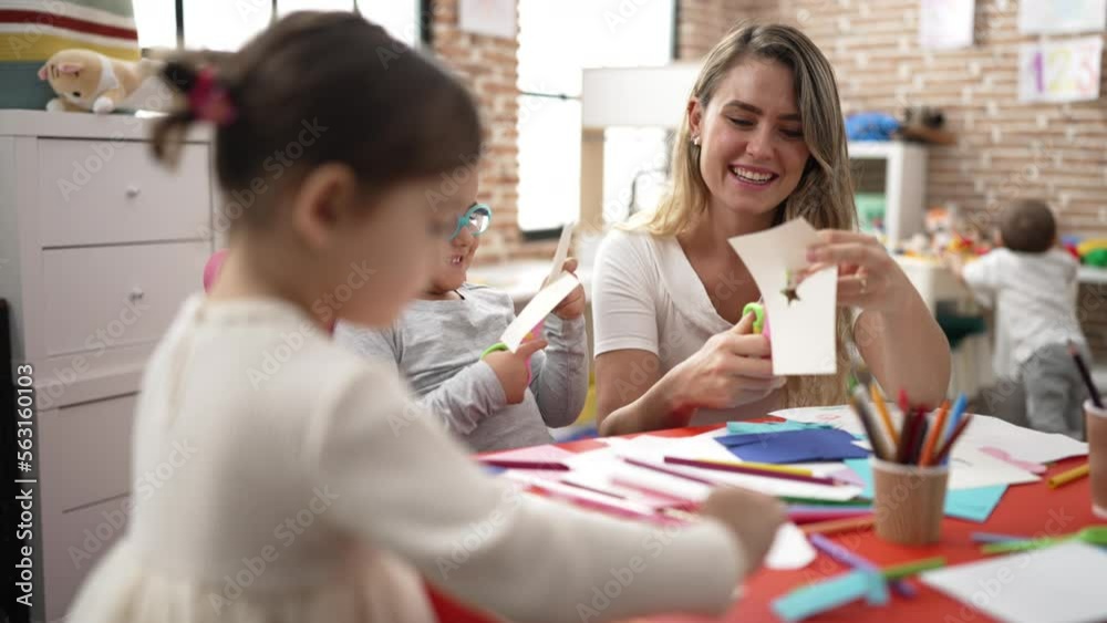 Teacher with boy and girl sitting on table having handcrafts class at kindergarten