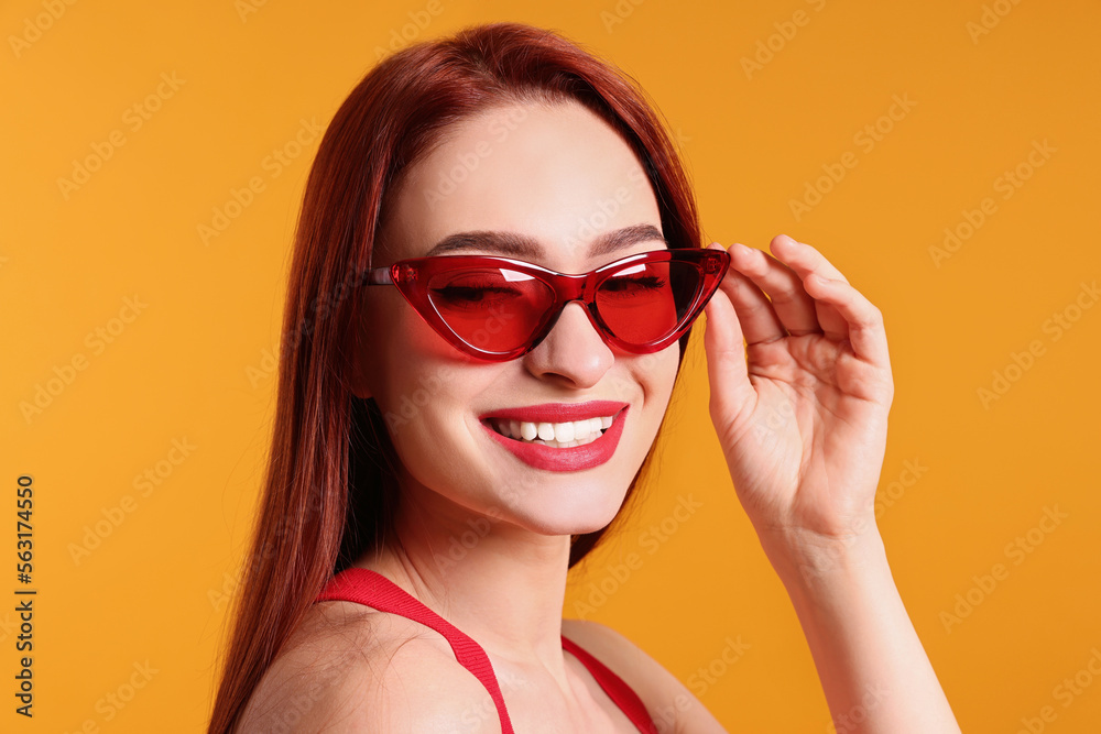 Fototapeta premium Happy woman with red dyed hair and sunglasses on orange background