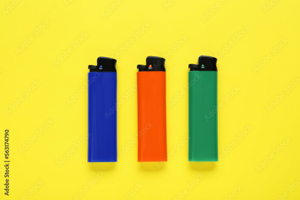 Stylish small pocket lighters on yellow background, flat lay Stylish small pocket lighters on yellow background, flat lay