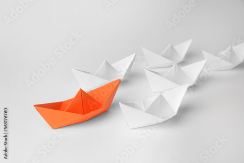 Group of paper boats following orange one on white background. Leadership concept