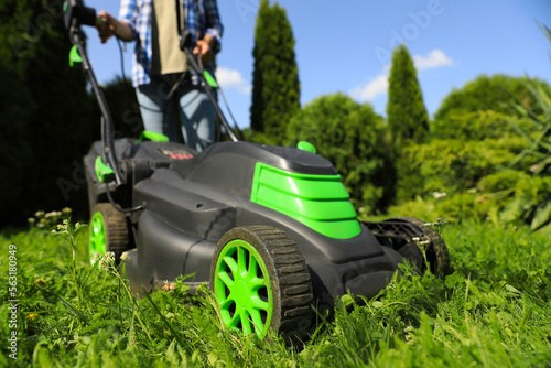 Woman turning on lawn mower in garden, closeup. Cutting grass