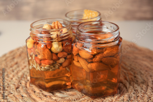 Jars with different nuts and honey on wicker mat, closeup