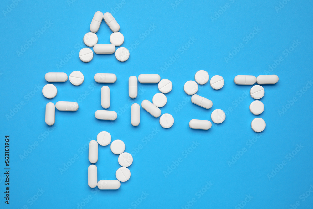 Words First Aid made of pills on light blue background, flat lay