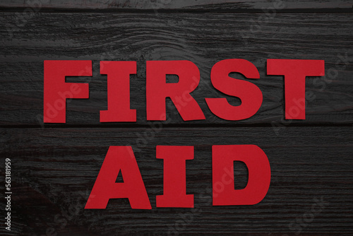 Words First Aid made of red letters on black wooden table, flat lay