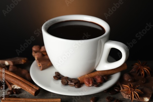 Cup of delicious hot chocolate, spices and coffee beans on wooden table