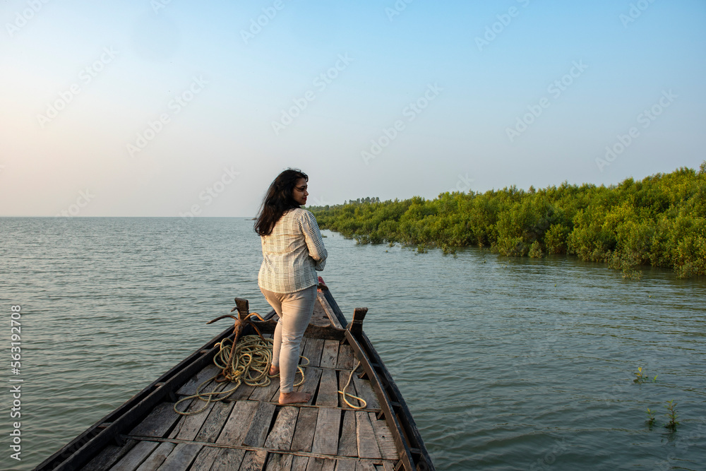 An young solo traveler standing on the adge of a country boat looking at the mangrove forest of Sundarban Tiger Reserve.