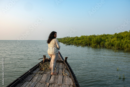 An young solo traveler standing on the adge of a country boat looking at the mangrove forest of Sundarban Tiger Reserve. photo