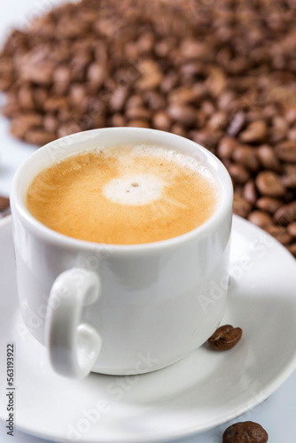 Fragrant coffee with foam in a white cup and grains scattered nearby. Traditional morning drink. Vertical. Top view.