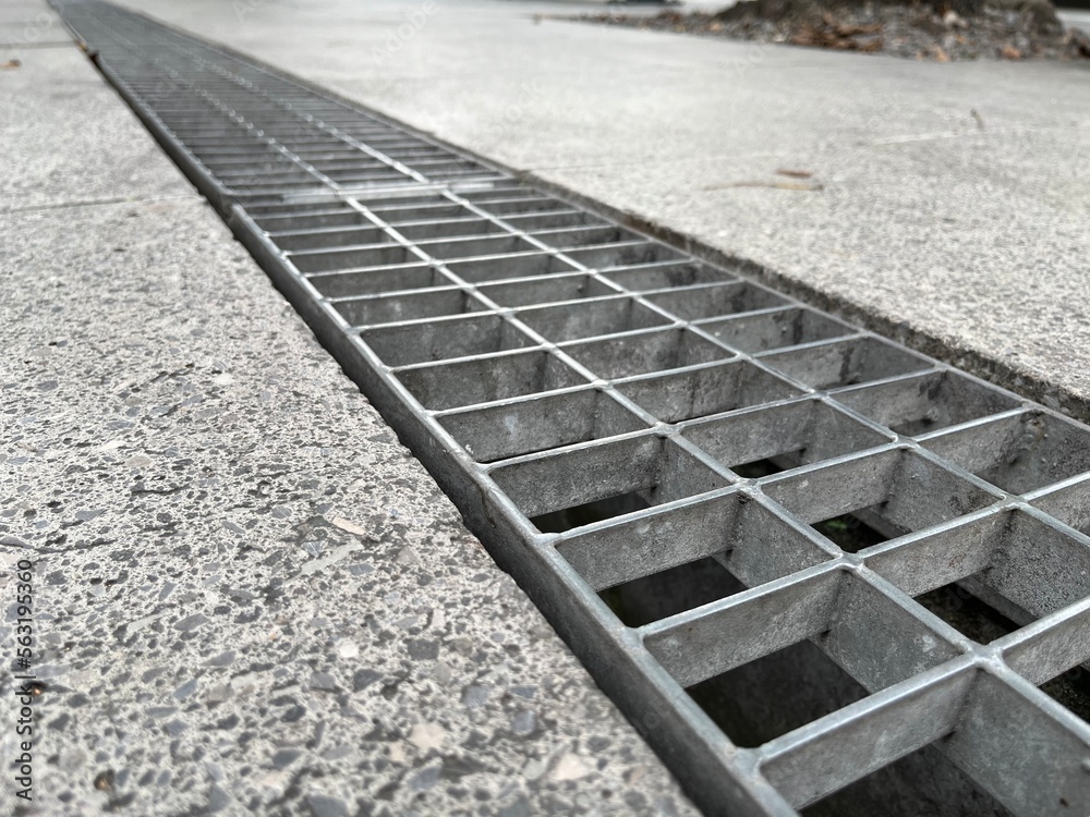 Obraz premium Closeup, metal cover of street water drain. Against the background of paving slabs made from gray granite