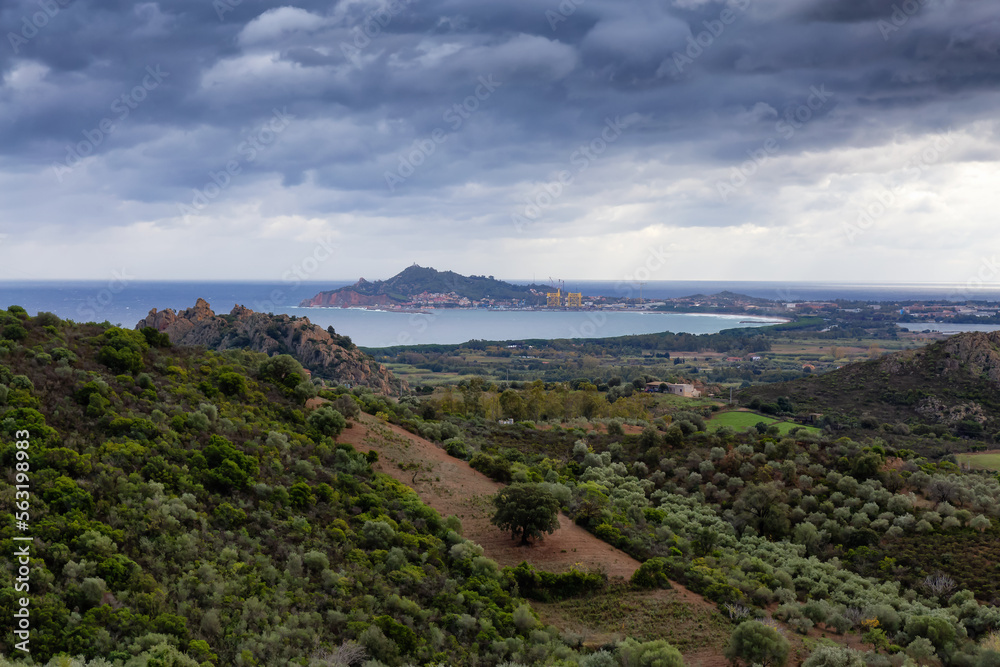 View of Farm Fields and Town on the Sea Coast. Santa Maria Navarrese, Sardinia, Italy. Cloudy and Rainy Sky.