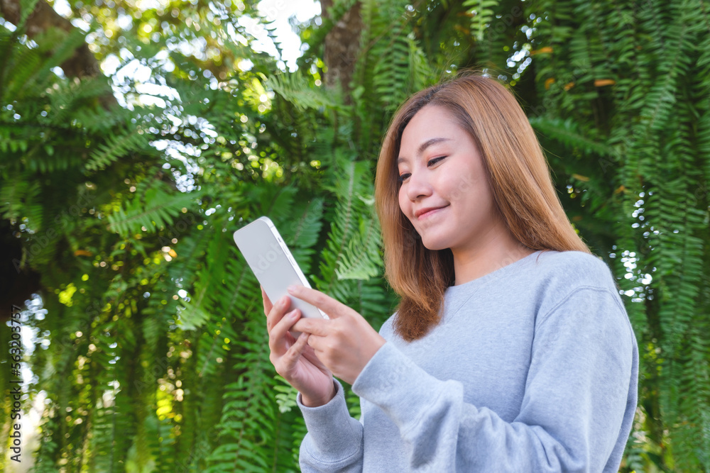 Portrait image of a beautiful young asian woman holding and using mobile phone in the outdoors Portrait image of a beautiful young asian woman holding and using mobile phone in the outdoors