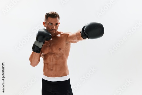 Man athletic bodybuilder poses in boxing gloves with nude torso abs in full-length background, boxing and martial arts. Advertising, sports, active lifestyle, competition, challenge concept.  © SHOTPRIME STUDIO