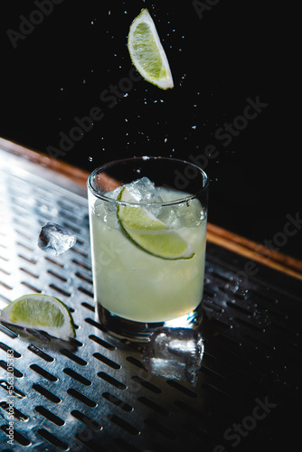 Classic Margarita with salt and lime falling around the glass on bar photo