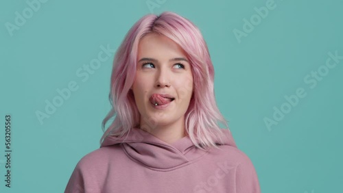Young fresh creative hipster girl 20s licking plump lips and blowing the air kiss looking straight in camera. Young playful woman face licking sexy lips and flirting. Attractive woman with pink hair
