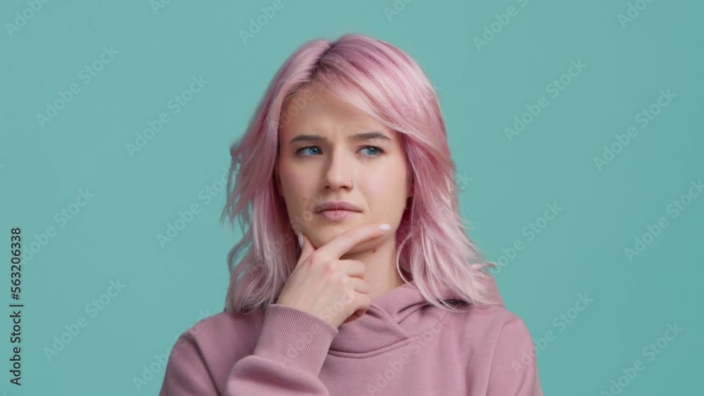 Clever student hipster girl with creative pink hair considering serious plan, solving problem in mind, thinking over smart idea, pondering and musing answer, indoor studio shot isolated on blue wall Clever student hipster girl with creative pink hair considering serious plan, solving problem in mind, thinking over smart idea, pondering and musing answer, indoor studio shot isolated on blue wall