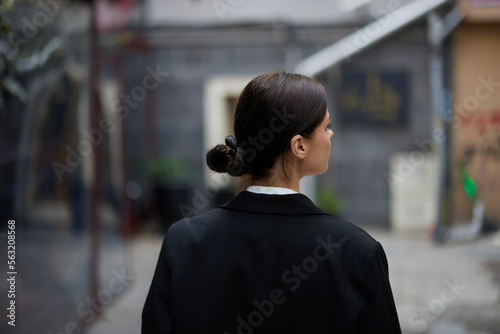 Stylish woman in a black jacket walks along the city street with her back to the camera, follow me