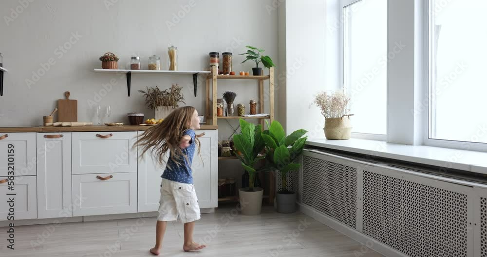 Cute little active preschooler girl spins, swirls, jumping barefoot on warm floor with underfloor heat system in modern kitchen at home, play feels happy looks carefree. Untroubled childhood, playtime Cute little active preschooler girl spins, swirls, jumping barefoot on warm floor with underfloor heat system in modern kitchen at home, play feels happy looks carefree. Untroubled childhood, playtime