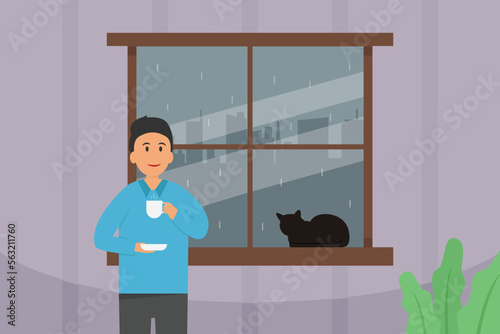 Young man drinking a cup of tea at home with raining season outside the window