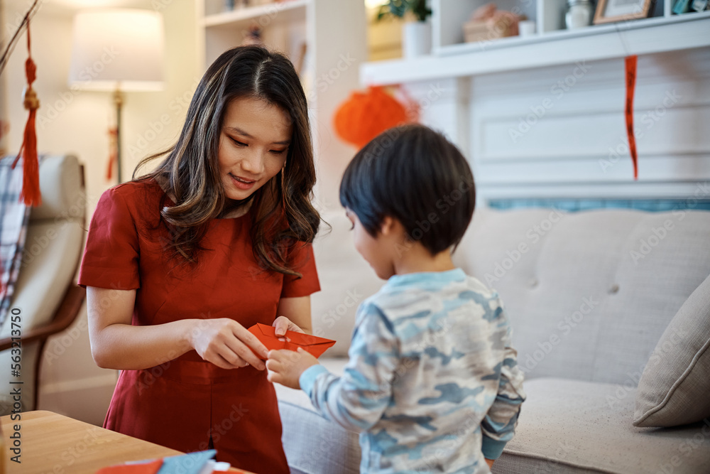 Chinese mother and son opening red envelope during New Year celebration at home.