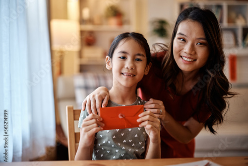 Happy Asian mother and daughter with traditional red envelope during Chinese New Year at home looking at camera.