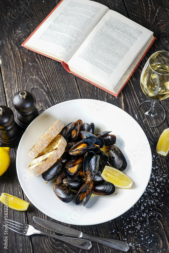boiled mussels in a plate with lemon and bruschetta on a table with a book and a glass of wine vertical photo

