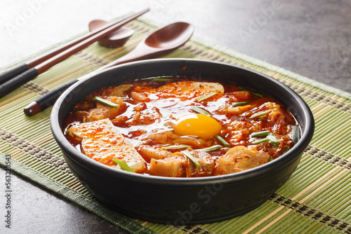 Sundubu-jjigae dish is made with freshly curdled soft tofu, kimchi, onion, pork belly and gochugaru closeup on the bowl on the table. Horizontal photo