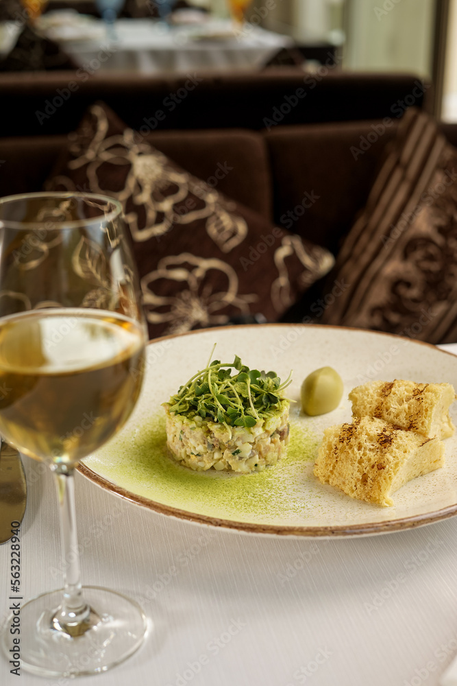 Olivier salad decorated with microgreens in a plate with porridge on the table with a glass of white wine, vertical photo
