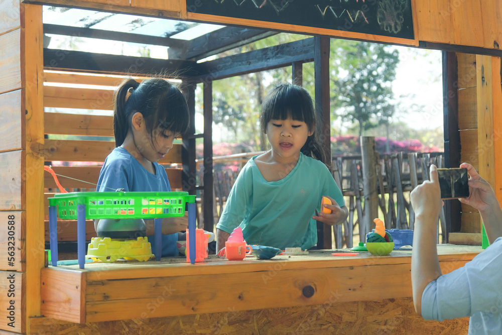 Φωτογραφία Two happy sisters play with food and wooden grocery toys at the outdoor playground with her mother