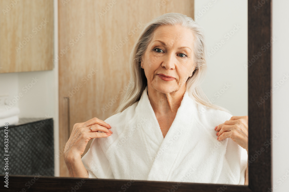 Senior woman adjusting her bathrobe in front of a mirror Senior woman adjusting her bathrobe in front of a mirror