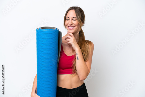 Young sport woman going to yoga classes while holding a mat isolated on white background looking to the side and smiling