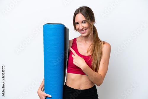 Young sport woman going to yoga classes while holding a mat isolated on white background pointing to the side to present a product