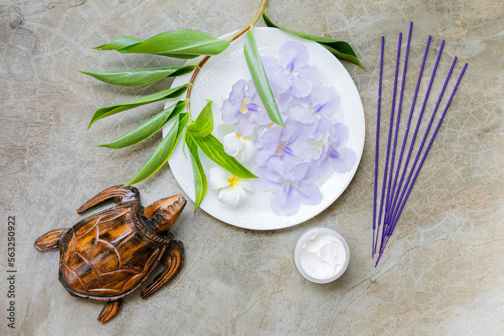 Incense sticks, natural face cream, wooden turtle, violet asian flowers on concrete background top view 