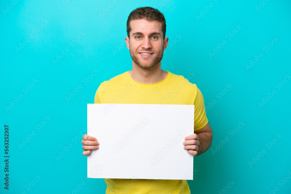 Young caucasian man isolated on blue background holding an empty placard with happy expression Young caucasian man isolated on blue background holding an empty placard with happy expression