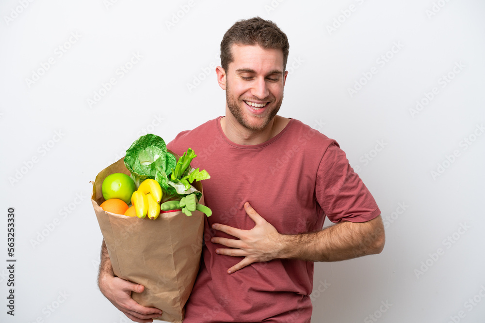 Young caucasian man holding a grocery shopping bag isolated on white background smiling a lot Young caucasian man holding a grocery shopping bag isolated on white background smiling a lot