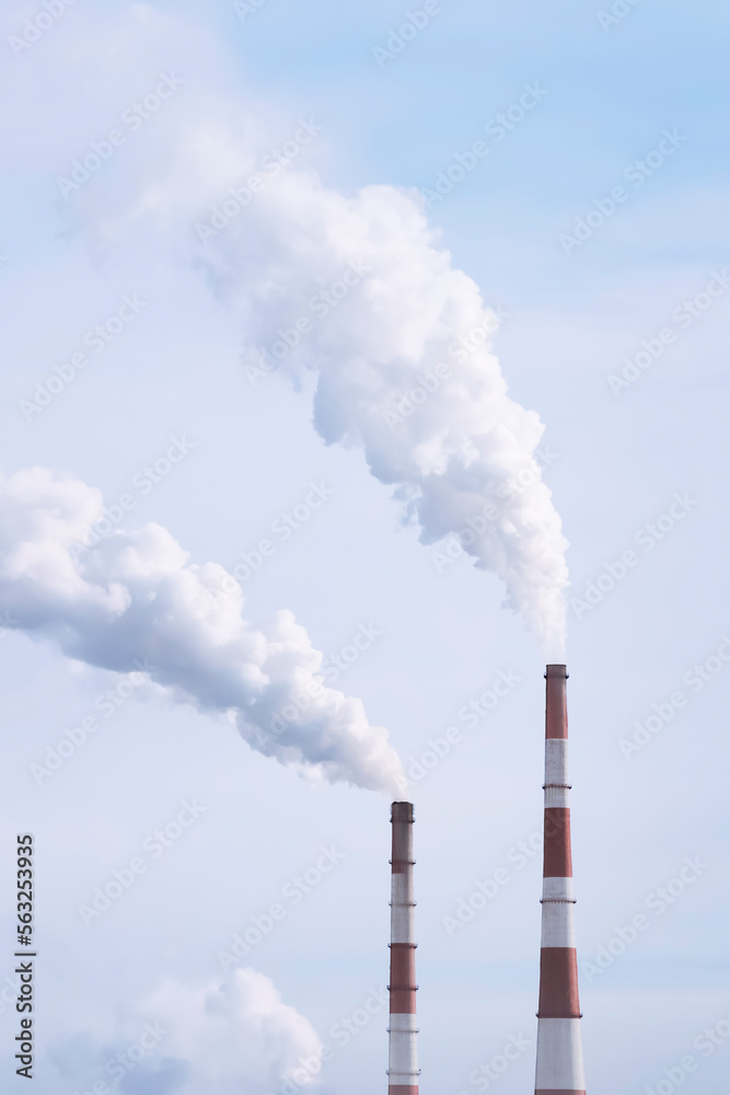 Thermal power plant with smoking chimneys against a cloudy sky. Vertical