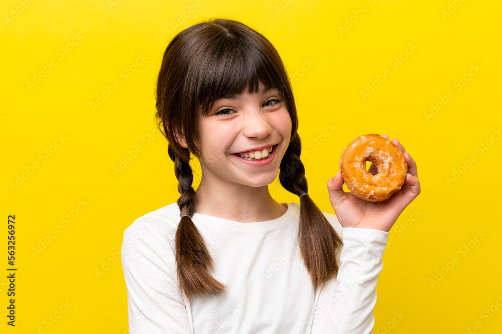 Little caucasian girl isolated on yellow background holding a donut and happy