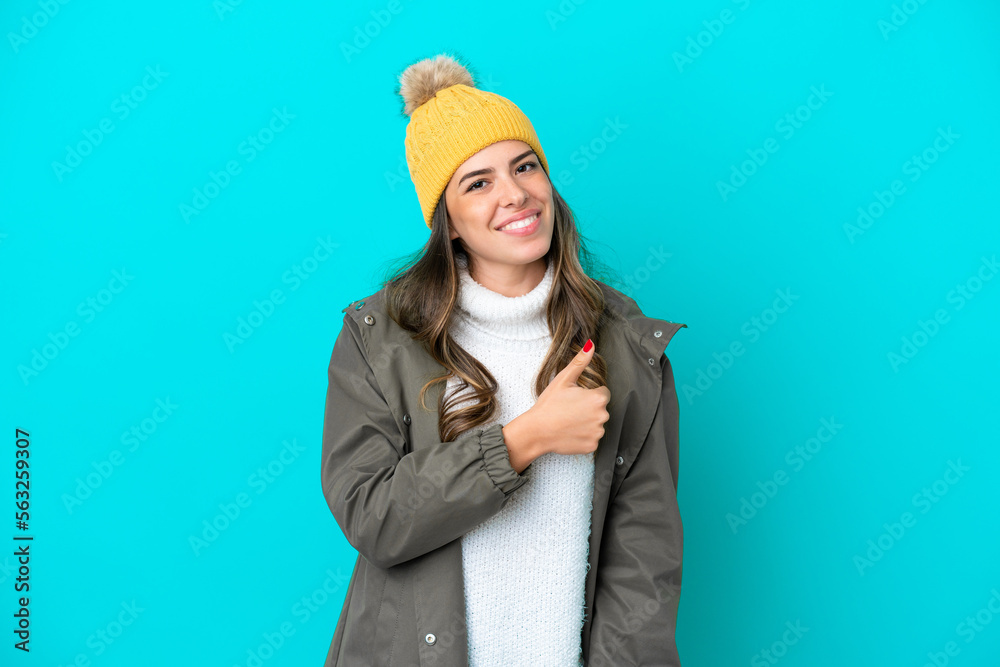 Young Italian woman wearing winter jacket and hat isolated on blue background giving a thumbs up gesture Young Italian woman wearing winter jacket and hat isolated on blue background giving a thumbs up gesture