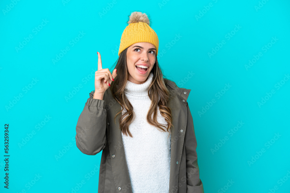 Young Italian woman wearing winter jacket and hat isolated on blue background intending to realizes the solution while lifting a finger up Young Italian woman wearing winter jacket and hat isolated on blue background intending to realizes the solution while lifting a finger up