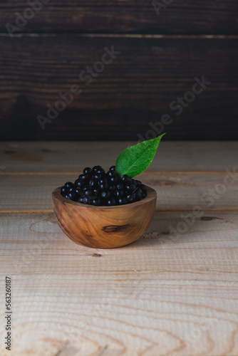 Fresh ripe elderberry in a wooden bowl on a wooden background side view. Wild berries.