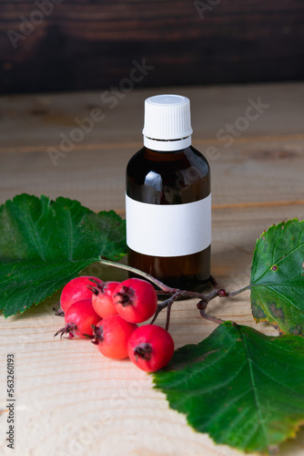 Glass bottle with tincture and ripe hawthorn berries on a wooden background.