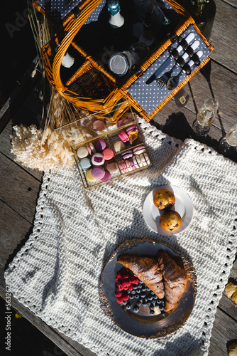 Picnic basket with bakery, fruits and sweets on white blanket.