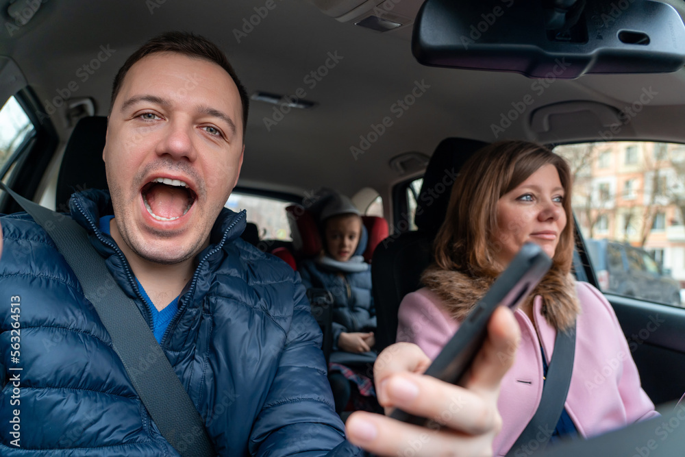 Woman is driving car with excited happy man sitting in passenger seat and looking at camera. Enjoying road trip together. Married couple with children on trip. Concept of travel, love and family