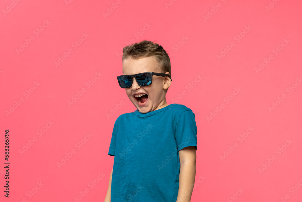 Little boy in sunglasses and blue t-shirt. He smiling, posing pink background. Childhood, fashion, advertising. Copy space Little boy in sunglasses and blue t-shirt. He smiling, posing pink background. Childhood, fashion, advertising. Copy space